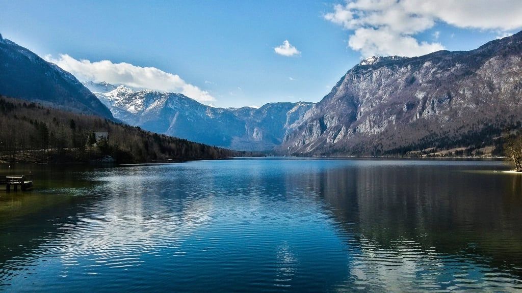 Besneeuwde Julische Alpen omringen het diepblauwe water van het Meer van Bohinj onder een heldere lucht in Nationaal park Triglav.
